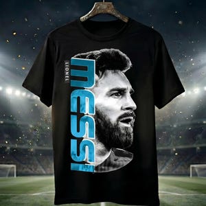 Puede incluir: Una camiseta negra de manga corta con un gran retrato en blanco y negro de Lionel Messi de perfil. El nombre MESSI est&aacute; impreso verticalmente en letras may&uacute;sculas de color azul claro junto al retrato, con la palabra LIONEL encima.