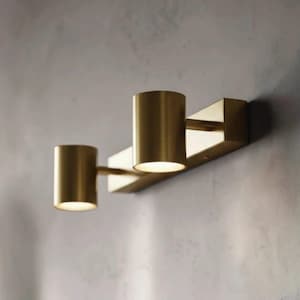 Puede incluir: Un aplique de pared con una placa base rectangular de latón y dos focos cilíndricos de latón. Cada foco está unido a la base mediante un brazo horizontal corto, con la fuente de luz dirigida hacia abajo desde los extremos abiertos.