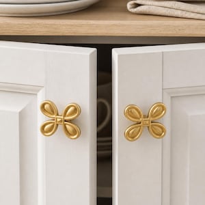 May include: Two white cabinet doors with gold-coloured, flower-shaped knobs. The knobs have a matte finish and are centred on the doors. The cabinet doors are slightly ajar, revealing a glimpse of the interior.
