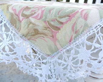 May include: A white crocheted lace tablecloth with a floral pattern in shades of pink, green, and brown.
