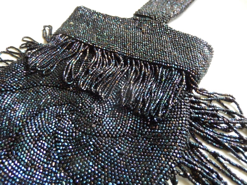 May include: A black beaded bag with a fringe detail. The beads have a slight iridescent sheen.