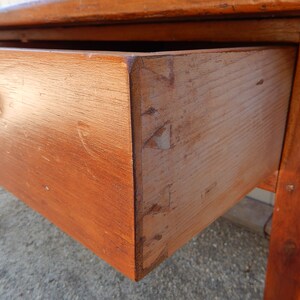 May include: A wooden table with a single drawer and turned knob. The table is made of solid wood and has a natural finish. The drawer is open and shows the wood grain.
