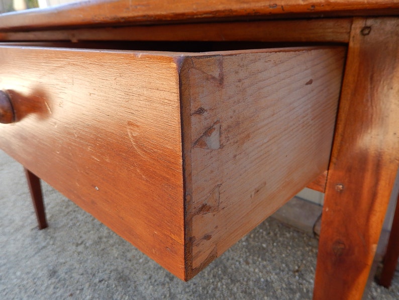 May include: A wooden table with a single drawer and turned knob. The table is made of solid wood and has a natural finish. The drawer is open and shows the wood grain.