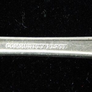 K&ouml;nnte beinhalten: Nahaufnahme der R&uuml;ckseite eines silbernen L&ouml;ffels mit der Gravur "Community Plate".