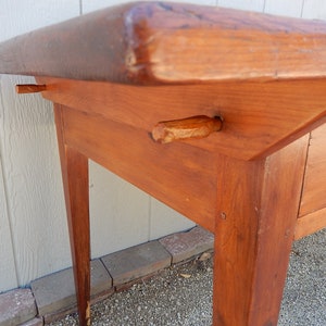 May include: A wooden table with a drawer and two legs. The table is made of solid wood and has a natural finish. The table is in good condition and has a rustic look.