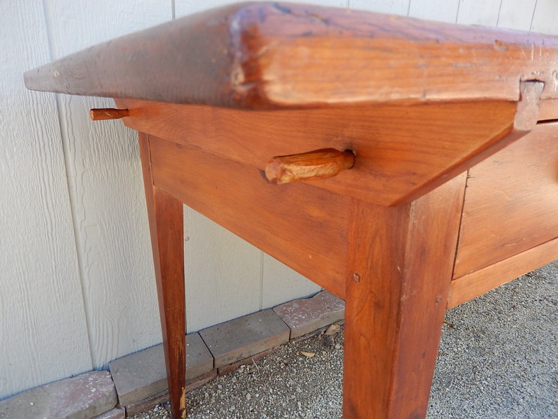 May include: A wooden table with a drawer and two legs. The table is made of solid wood and has a natural finish. The table is in good condition and has a rustic look.