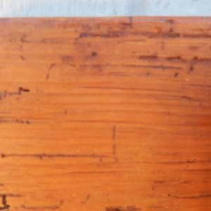 May include: Close-up of a wooden surface with a natural wood grain pattern. The surface is a light brown color with a slightly orange hue. The wood has a rustic appearance with visible knots and imperfections.