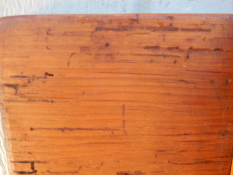 May include: Close-up of a wooden surface with a natural wood grain pattern. The surface is a light brown color with a slightly orange hue. The wood has a rustic appearance with visible knots and imperfections.
