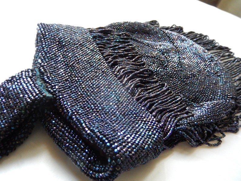 May include: A vintage beaded purse with a dark blue iridescent finish and a fringe detail.