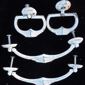 May include: A collection of white, distressed-finish cabinet hardware. The set includes two ring-pull handles and two pairs of curved handles, all with decorative detailing. The hardware is designed for furniture restoration or new builds.