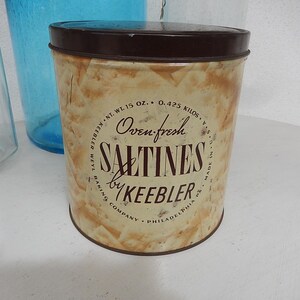 Può includere: Latta vintage di Saltines Keebler con coperchio marrone e corpo beige e marrone. La latta riporta "Oven Fresh Saltines by Keebler" e include il peso, 425 grammi.