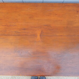 May include: A close-up of a wooden table top with a natural wood finish. The table top has three decorative inlays in the shape of a bow tie.