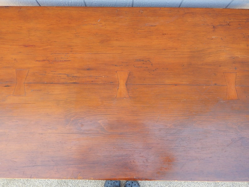 May include: A close-up of a wooden table top with a natural wood finish. The table top has three decorative inlays in the shape of a bow tie.