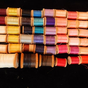 Pu&ograve; includere: Una collezione di bobine di filo di vari colori, tra cui rosso, rosa, blu, verde, giallo e marrone. Le bobine sono disposte in fila e tutte avvolte con filo.