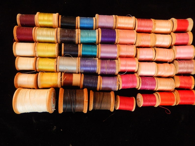 Pu&ograve; includere: Una collezione di bobine di filo di vari colori, tra cui rosso, rosa, blu, verde, giallo e marrone. Le bobine sono disposte in fila e tutte avvolte con filo.