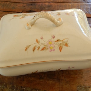 May include: White ceramic serving dish with a lid and two handles. The lid has a floral design with pink and yellow flowers and brown leaves. The dish has a gold trim around the edge.