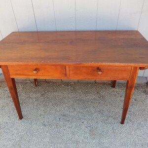 May include: A wooden table with two drawers and four legs. The table is made of a light brown wood and has a simple design.