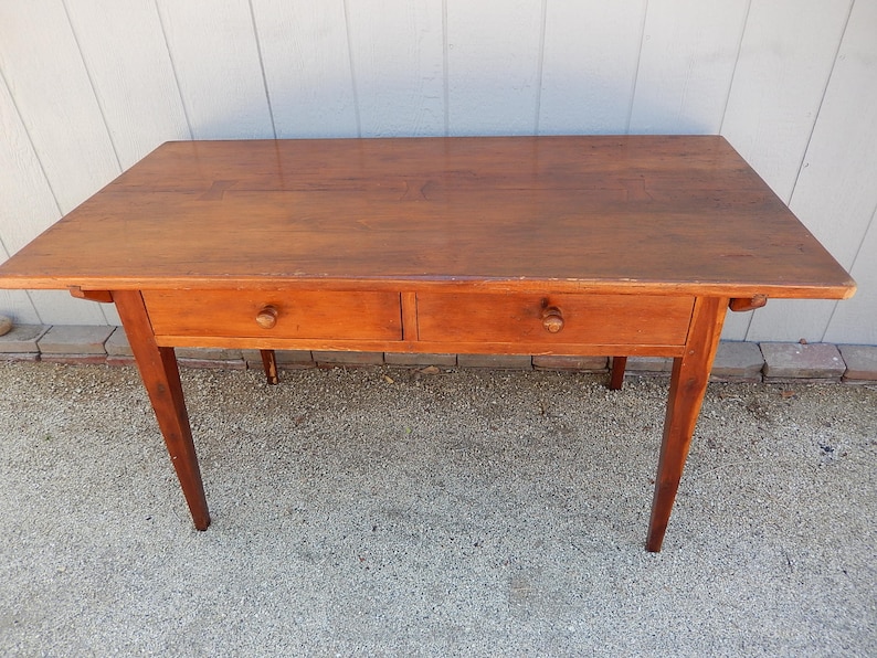 May include: A wooden table with two drawers and four legs. The table is made of a light brown wood and has a simple design.