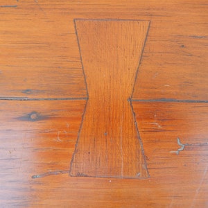 May include: Close-up of a wooden table top with a unique, geometric inlay in the shape of a bow tie. The inlay is made of the same wood as the table top, but it is a slightly different shade.