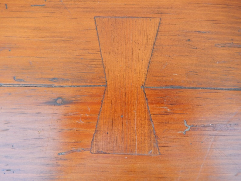 May include: Close-up of a wooden table top with a unique, geometric inlay in the shape of a bow tie. The inlay is made of the same wood as the table top, but it is a slightly different shade.