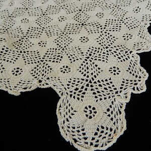 May include: A close-up of a white crocheted doily with a delicate floral pattern. The doily is made with a fine thread and has a scalloped edge.