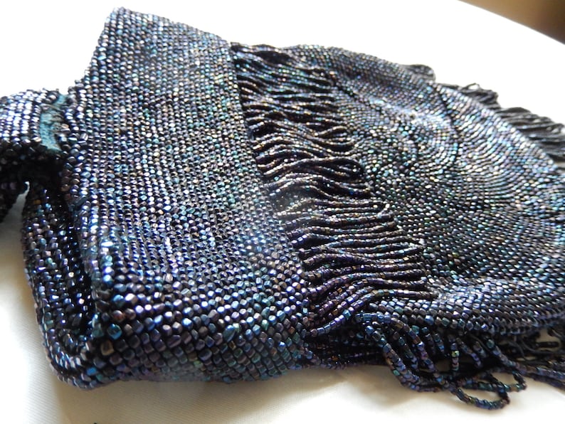 May include: A vintage beaded evening bag with a fringe detail. The bag is made of iridescent blue beads and has a rectangular shape.