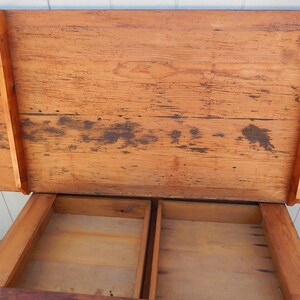 May include: A wooden table with a lift-up top and two drawers. The table is made of natural wood with a rustic finish. The top of the table is open and the drawers are empty.