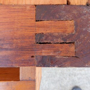 May include: Close-up of a wooden corner joint with three visible slots. The wood is a dark brown color and shows signs of wear and age.