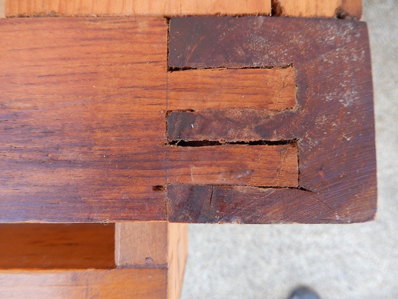 May include: Close-up of a wooden corner joint with three visible slots. The wood is a dark brown color and shows signs of wear and age.