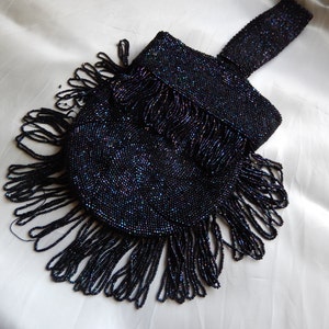 May include: A black beaded evening bag with a fringe detail. The bag is made of small, iridescent beads and has a long, beaded strap.
