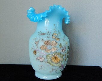 Könnte beinhalten: Eine hellblaue Glasvase mit einem gekräuselten Rand und einem Blumendesign in Gold, Rosa und Grün.