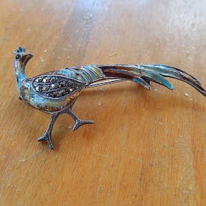 May include: Vintage silver-tone bird brooch with marcasite accents. The bird has a long tail and is detailed with blue and brown enamel. A classic piece of jewelry.