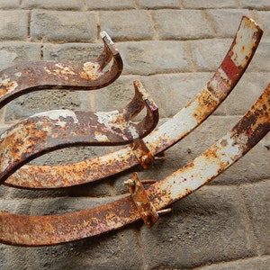 Può includere: Tre cerchi di metallo arrugginiti, dipinti di bianco con accenti rossi, sono impilati uno sopra l'altro. I cerchi sono curvi e hanno un aspetto usurato e invecchiato.