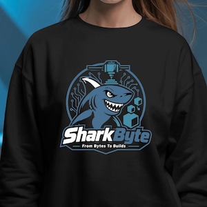 May include: A black long-sleeve sweatshirt featuring a graphic of a blue shark with a circuit board pattern in the background. Above the shark is a 3D printer nozzle icon. The text reads SharkByte and From Bytes To Builds in white and blue.