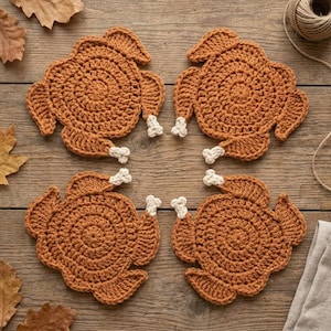 Peut inclure: Un ensemble de quatre dessous de verre au crochet marron en forme de dindes rôties, chacun présentant un corps circulaire, des ailes et de petits accents en fil blanc aux extrémités des pattes pour représenter les os, disposés en carré.