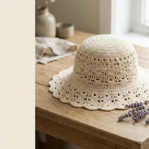 Peut inclure: Un chapeau en crochet de couleur crème doté d'une calotte arrondie et d'un large bord festonné. Le chapeau est réalisé avec des motifs ajourés complexes sur tout le corps et un détail de bordure en dentelle délicate sur le pourtour.