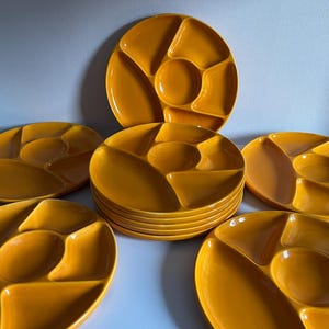 Peut inclure: Ensemble de plateaux de service en céramique jaune moutarde. Chaque plateau est divisé en cinq sections, avec un puits central circulaire. Les plateaux sont disposés de manière attrayante, mettant en valeur leur design et leur couleur.