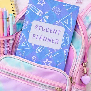 May include: A pastel-colored backpack with a student planner inside. The planner has a blue cover with white illustrations and the words "STUDENT PLANNER". Pens, a notepad, and school supplies surround the backpack.