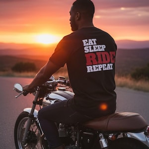 May include: A person on a motorcycle, wearing a black t-shirt with the words "EAT SLEEP RIDE REPEAT" in white and red. The motorcycle is silver and brown, set against a sunset backdrop.
