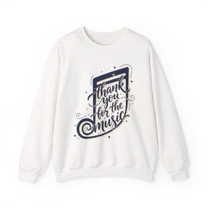 May include: White sweatshirt with a musical note design. The design features the text "Thank you for the music" in a stylized script, with navy blue and gold accents. The sweatshirt has a crew neck and long sleeves.