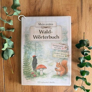 Könnte beinhalten: Ein Kinderbuch mit dem Titel "Mein erstes Wald-Wörterbuch". Das Cover zeigt Illustrationen eines schwarzen Spechts, eines rotkappigen Pilzes und eines Eichhörnchens. Das Buch ist mit einem Metallring gebunden und trägt die Aufschriften "Handgemacht mit Liebe" und "Fördert Sprache & Motorik".