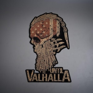 May include: A rectangular patch featuring a stylized skull with a braided beard and a top-knot hairstyle. The skull is overlaid with a distressed American flag pattern in muted red, white, and blue. Below the skull, the text reads UNTIL VALHALLA.