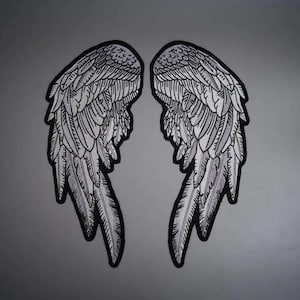 May include: A pair of embroidered patches featuring detailed angel wings in shades of black, white, and gray. The design showcases intricate feather patterns with bold black outlines, creating a symmetrical graphic representation of wings.