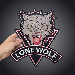 May include: An embroidered patch featuring a snarling grey wolf head with yellow eyes and an open mouth showing teeth and a pink tongue. The design is set against a black triangular background with red trim and a banner below reading LONE WOLF.