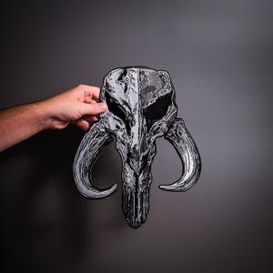 May include: A large embroidered patch featuring a stylized creature skull with prominent curved tusks. The design is rendered in shades of silver, grey, and black, with intricate textured stitching that creates a weathered, bone-like appearance.