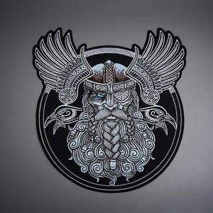 May include: A circular embroidered patch featuring a detailed illustration of a bearded figure wearing a winged helmet and an eye patch. The design uses black, white, and light blue thread to depict intricate knotwork patterns and two ravens.