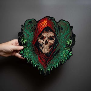 May include: An embroidered patch featuring a central skull with a beige and brown finish, draped in a vibrant red hood. The design is surrounded by intricate, flowing green foliage patterns against a black background with a die-cut edge.