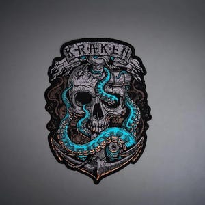 May include: A decorative patch featuring a detailed illustration of a human skull entwined with bright teal octopus tentacles. A large metal anchor sits at the base, and a banner at the top displays the word KRAKEN in bold black capital letters.