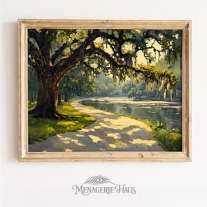 Puede incluir: Una pintura de paisaje enmarcada representa una serena escena junto al agua. Un camino sinuoso conduce a lo largo de un lago, sombreado por un gran árbol con musgo colgante. La obra de arte presenta una paleta de colores cálidos con verdes, marrones y amarillos, y está enmarcada en un marco de madera clara.