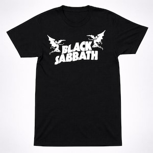 May include: A white ceramic mug with a black handle and the text "But First, Coffee" in a black, handwritten-style font. The mug is on a white surface.